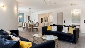 Ein modernes Wohnzimmer mit einer schwarzen Couch, gelben Kissen und einem Essbereich mit weißem Tisch und Stühlen.
