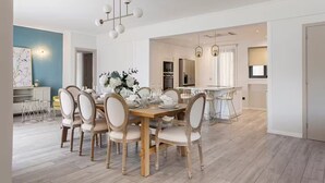 Ein moderner Essbereich mit einem Holztisch und Stühlen, im Hintergrund eine Küche und Pendelleuchten.