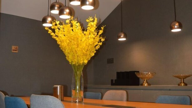 A dining area with a wooden table, chairs, a vase with yellow flowers, and pendant lighting.