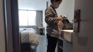A person pouring water into a cup near a sink in a hotel room.