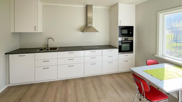 A modern kitchen with white cabinets, a stainless steel sink, and a built-in oven. - 1 bedroom nice apartment in Kvås (Kvås)