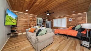 Una habitación acogedora con techo de madera, un sofá, una cama, un televisor y una kitchenette.