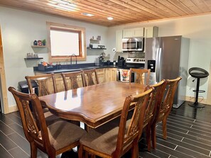 A modern kitchen with wooden cabinetry, a dining table with chairs, a coffee machine, and a refrigerator. - Private Spacious Cabin Retreat • Sleeps 17 • 3 Full Baths • Perfect for Groups (Crossville)