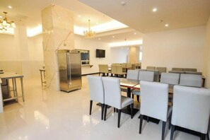 Uma área de refeições moderna com uma mesa central, cadeiras, um refrigerador e uma TV fixada na parede.