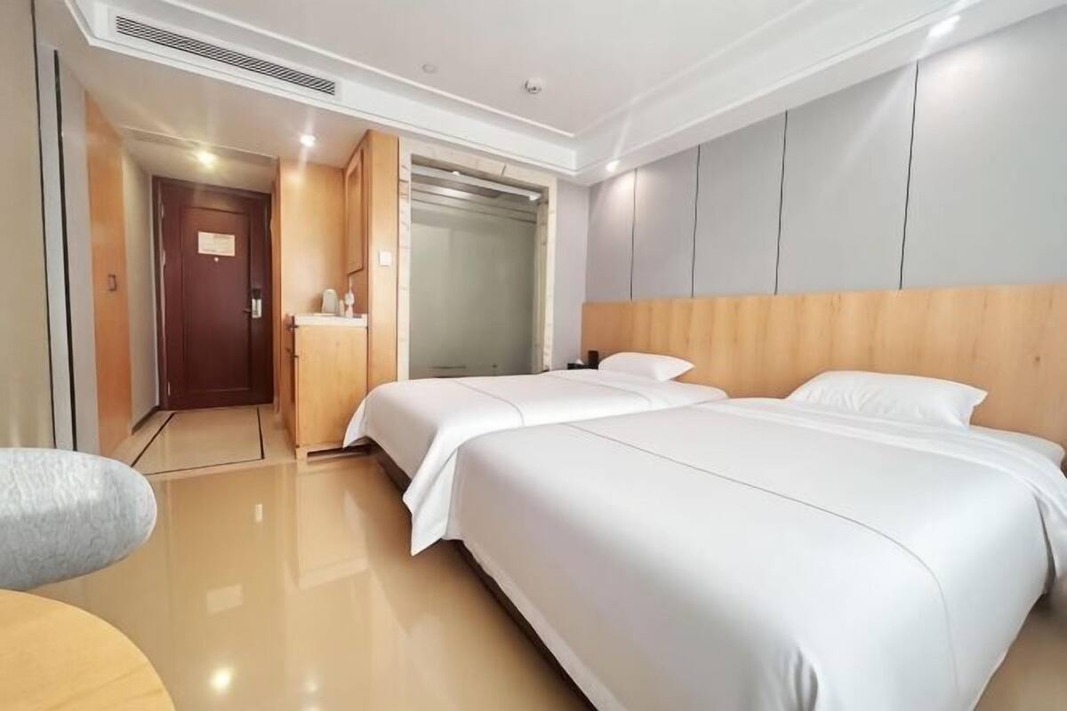 A hotel room with two beds, a wooden headboard, a mirror, a door, and a small table.