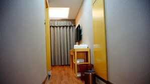 A narrow hallway with a skylight, a wooden bench with a towel, a trash bin, and a television on the wall.