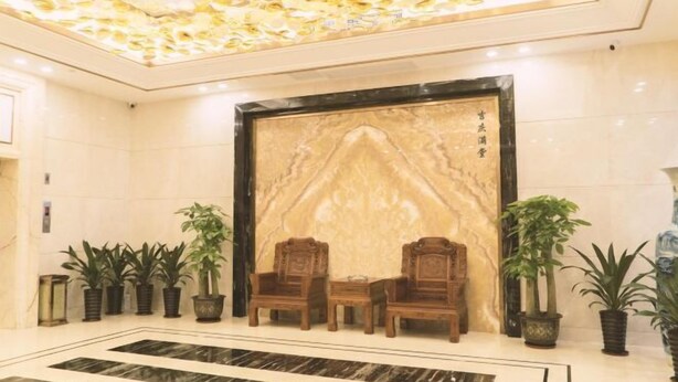 A lobby with a marble wall, two wooden chairs, and potted plants.