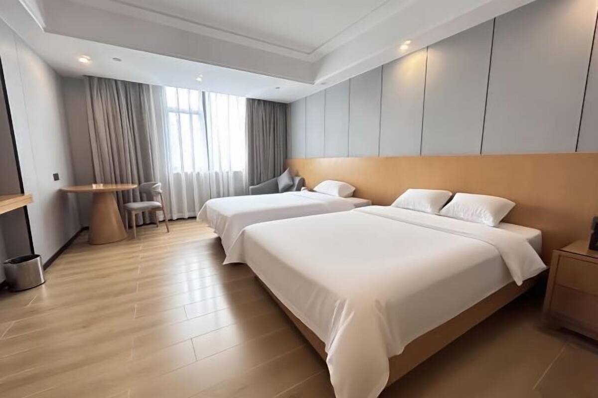 A modern hotel room with two beds, a round table, and a small seating area.