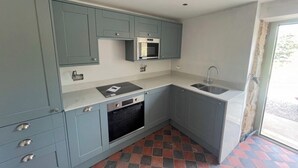 Una cocina compacta con armarios grises, horno empotrado, microondas y lavabo.