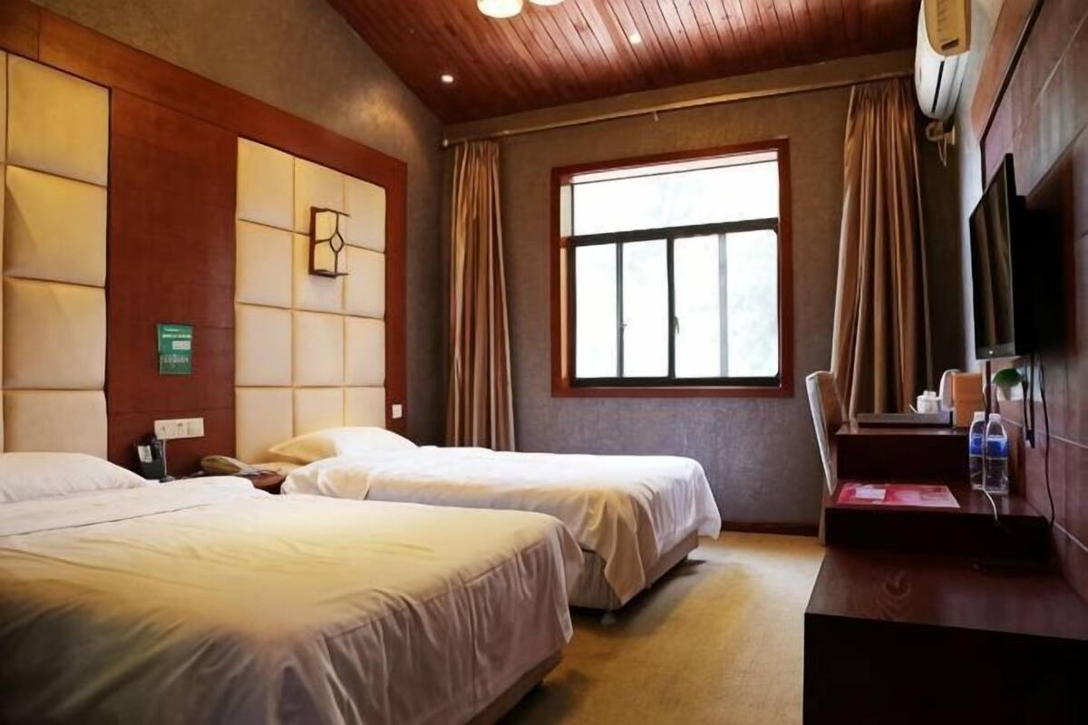 A hotel room with two beds, a desk, a window, and a television.