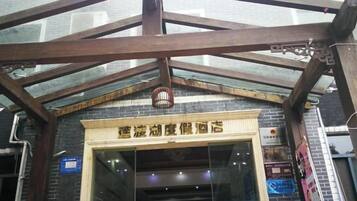 A hotel entrance with a glass facade, wooden beams, and a sign above the door.