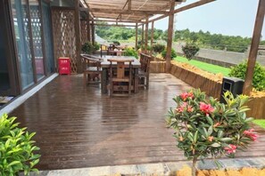 Una terraza de madera al aire libre con una mesa y sillas, rodeada de plantas y vistas al paisaje.