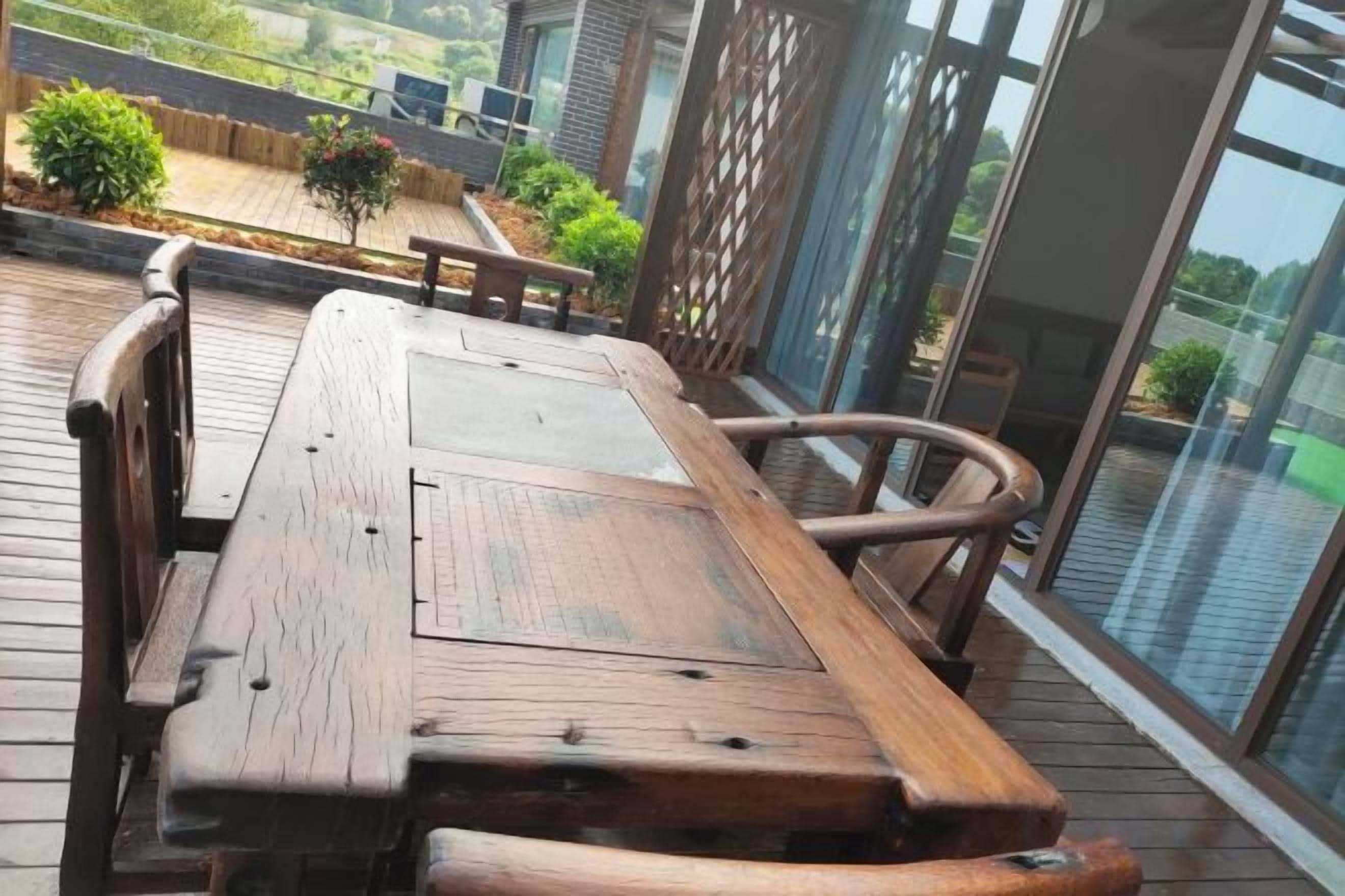 Terraza de madera con mesa y sillas, con vistas a un jardín y un edificio.