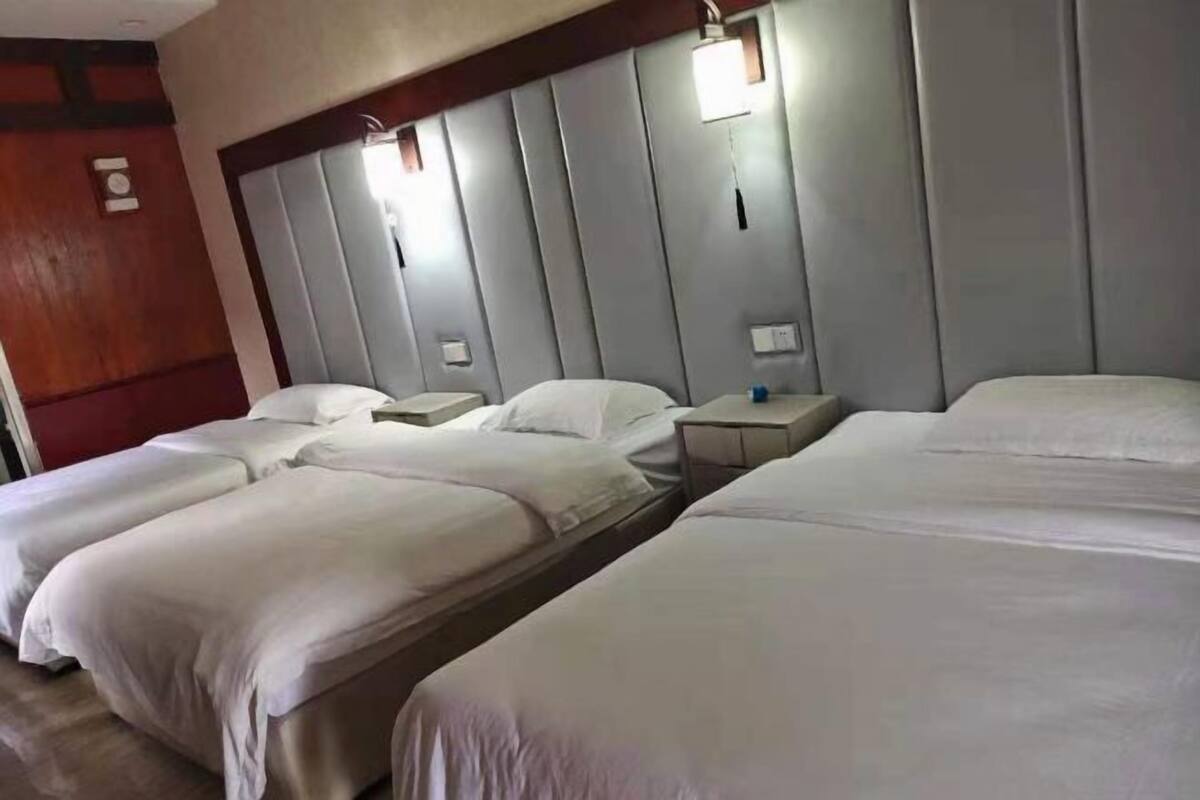 A hotel room with three beds, a wooden headboard, bedside tables, and a wall-mounted light fixture.