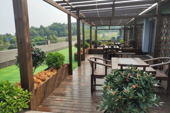 An outdoor patio with wooden flooring, tables, chairs, and potted plants.