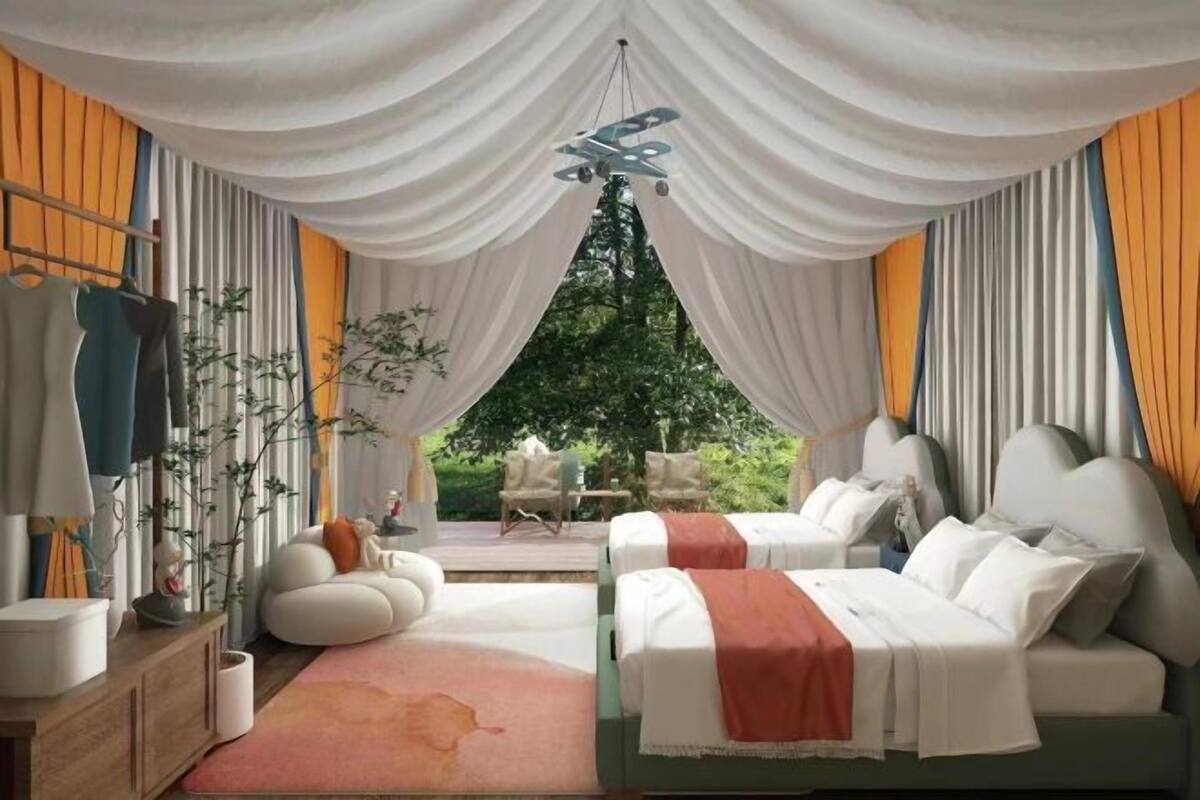A bedroom with two beds, a wooden side table, a hanging light fixture, and a view of the outdoors.