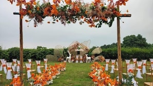 Un lugar para bodas al aire libre con un arco floral y una estructura rústica que recuerda a un granero al fondo.