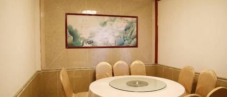 A conference room with a round table and chairs, a painting on the wall, and a tiled floor.