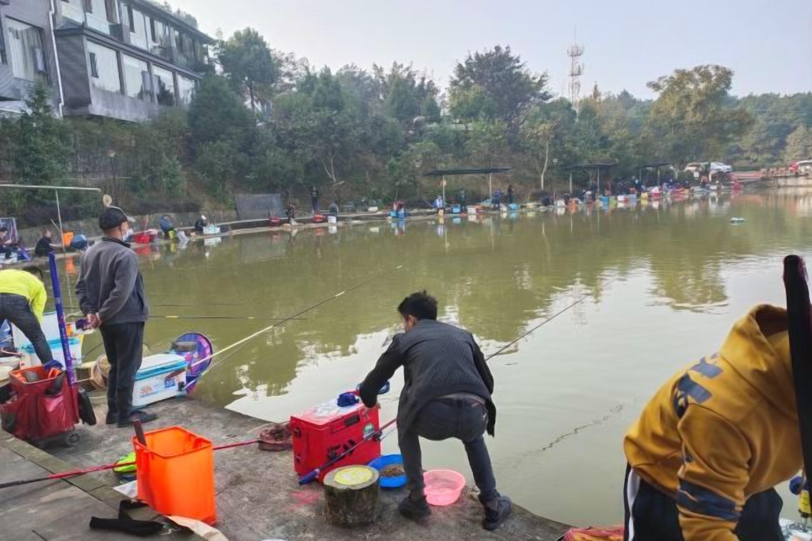 Un grupo de personas junto a un cuerpo de agua, algunas sosteniendo cañas de pescar.