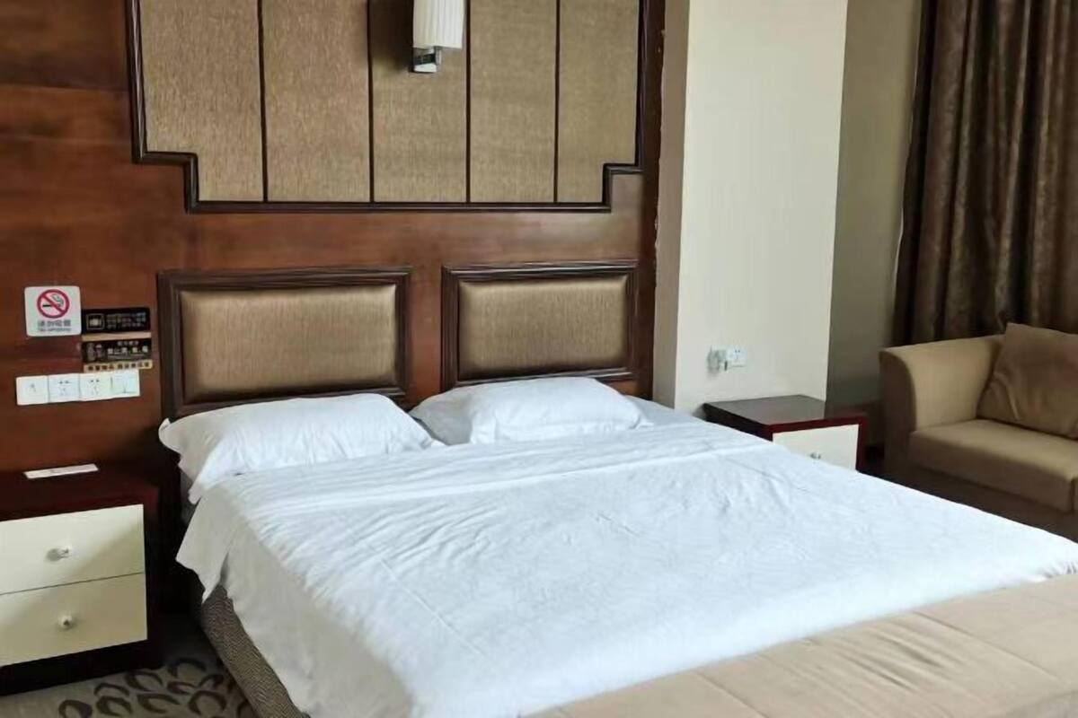 A hotel room with a bed, nightstands, a sofa, a wall-mounted light, and a no-smoking sign.