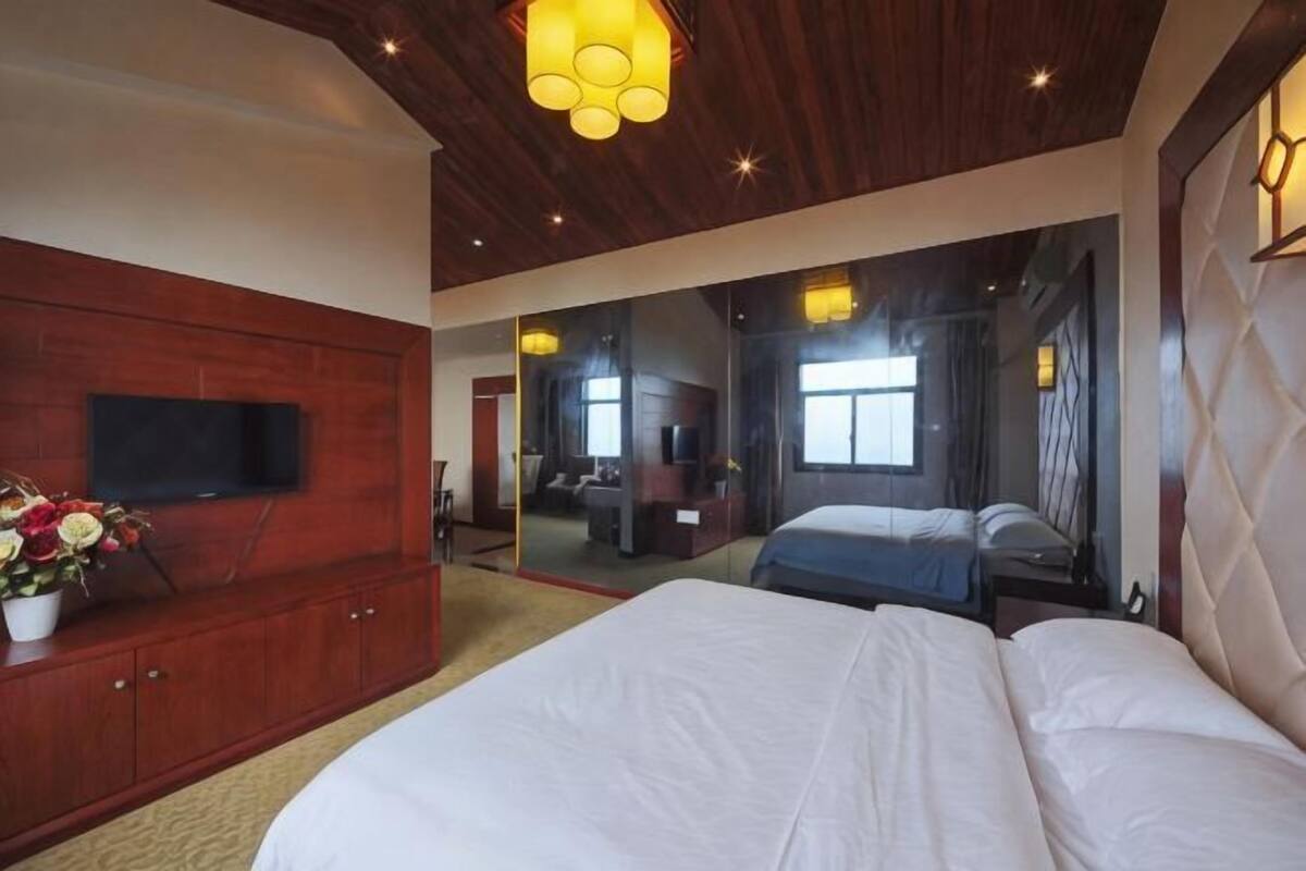 A bedroom with a large bed, a TV on a wooden cabinet, and a mirror reflecting the room.