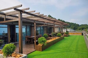 Un área de estar al aire libre con techado, mesas y sillas, un césped y vistas del paisaje.