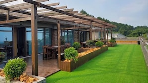 Un área de comedor al aire libre techada con pérgolas de madera, mesas y macetas.