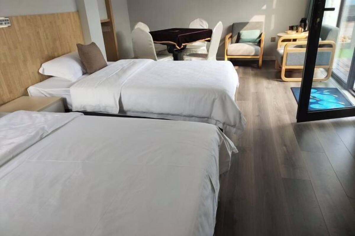 A hotel room with two beds, a dining table, chairs, and a view through a glass door.