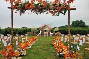 Un lieu de réception en plein air pour les mariages, agrémenté d’une arche fleurie, de chaises disposées en rangées et d’un décor composé d’une structure ornementale.