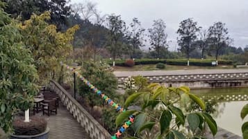 Un vialetto lastricato con ringhiera, un'area relax con tavoli e vista su uno specchio d'acqua e vegetazione.