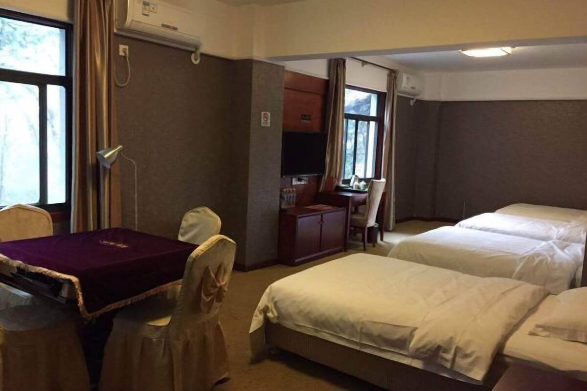 A hotel room with two beds, a desk, a chair, a table with a purple tablecloth, and a TV.
