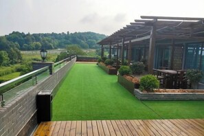 A wooden deck with a green artificial turf lawn, a pergola structure, and a view of a forested area. - Chongqing Liandu Lake Resort (Chongqing)