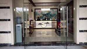 Un área de recepción con puerta de vidrio, dispensador de agua y un mural de un paisaje con flores.
