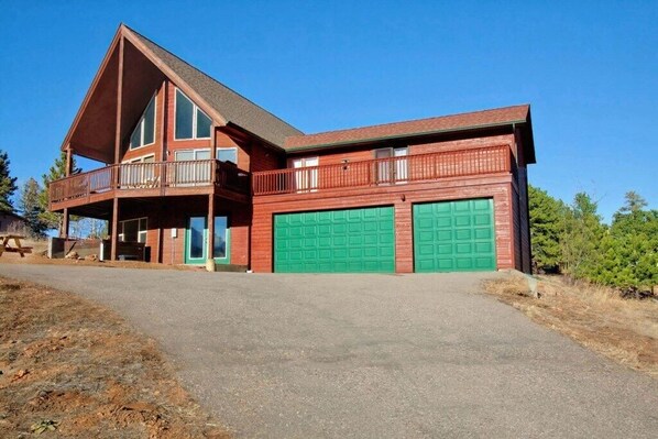 A two-story house with a balcony, a covered porch, and two green garage doors.