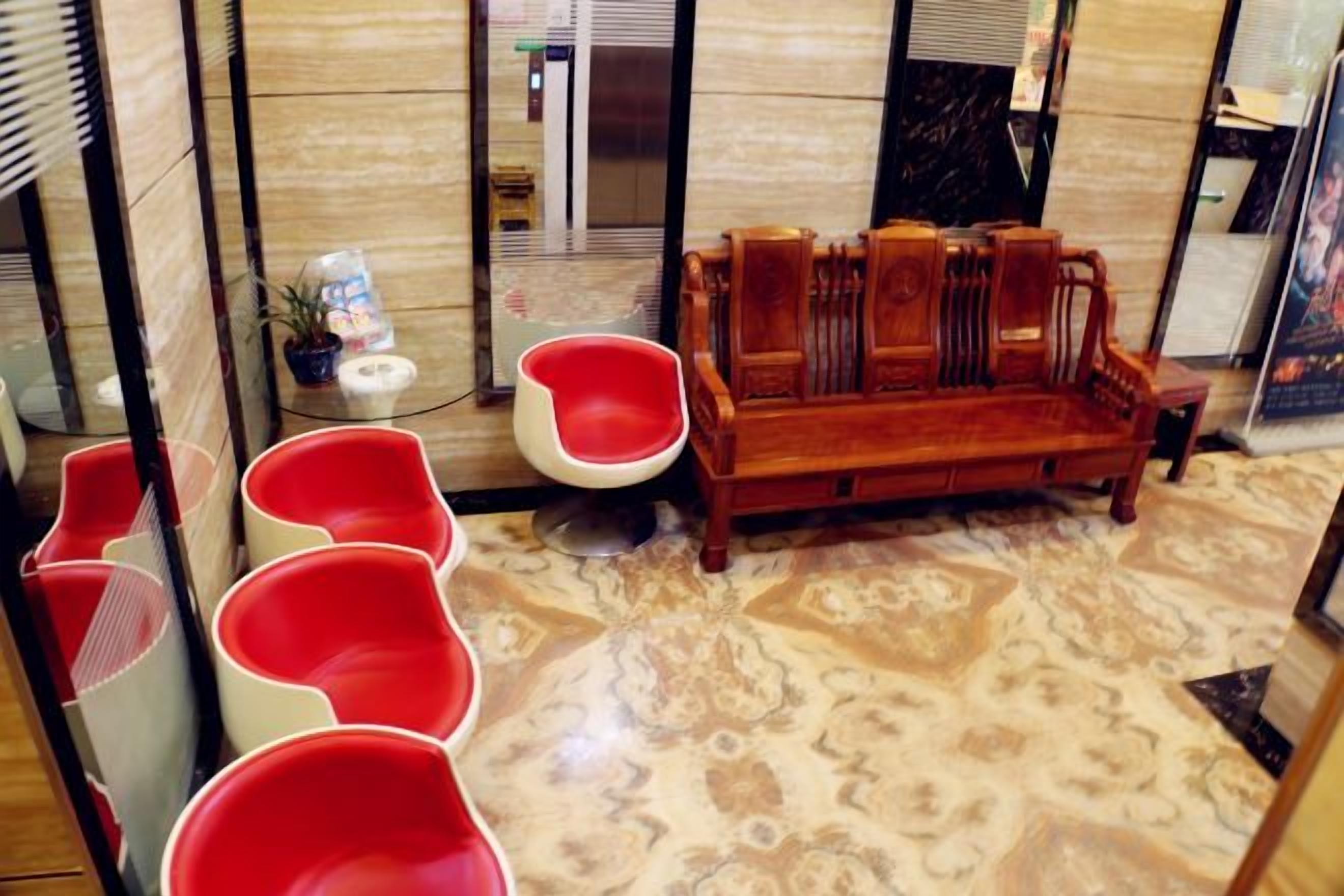 Una habitación con piso estampado, un sofá de madera y sillas rojas.