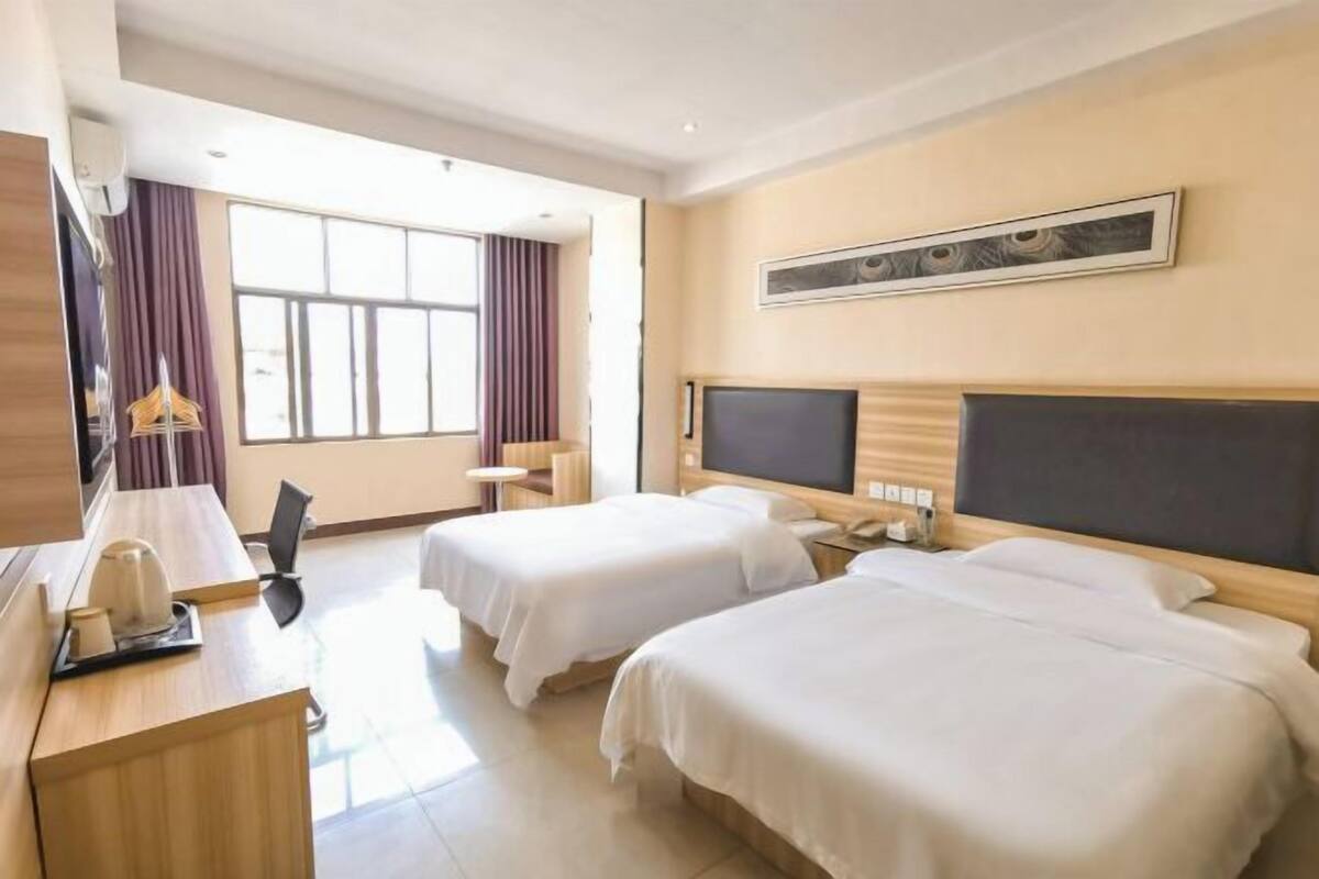 A hotel room with two beds, a desk with a telephone, a TV, and a window with curtains.