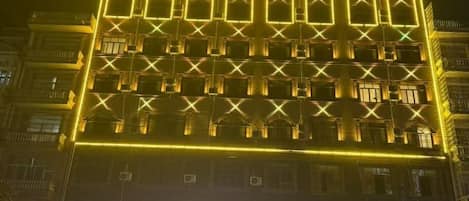 Un edificio de varios pisos con fachada de diseño geométrico, iluminado por luces amarillas.
