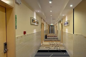 Ein Hotelgang mit Teppichstufen, Türen auf beiden Seiten und gerahmten Bildern an den Wänden.