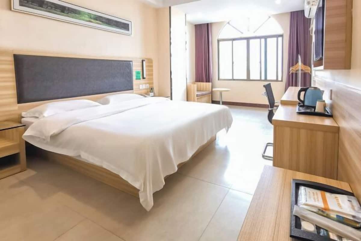 A hotel room with a large bed, a desk, a chair, a small table, and a window with curtains.