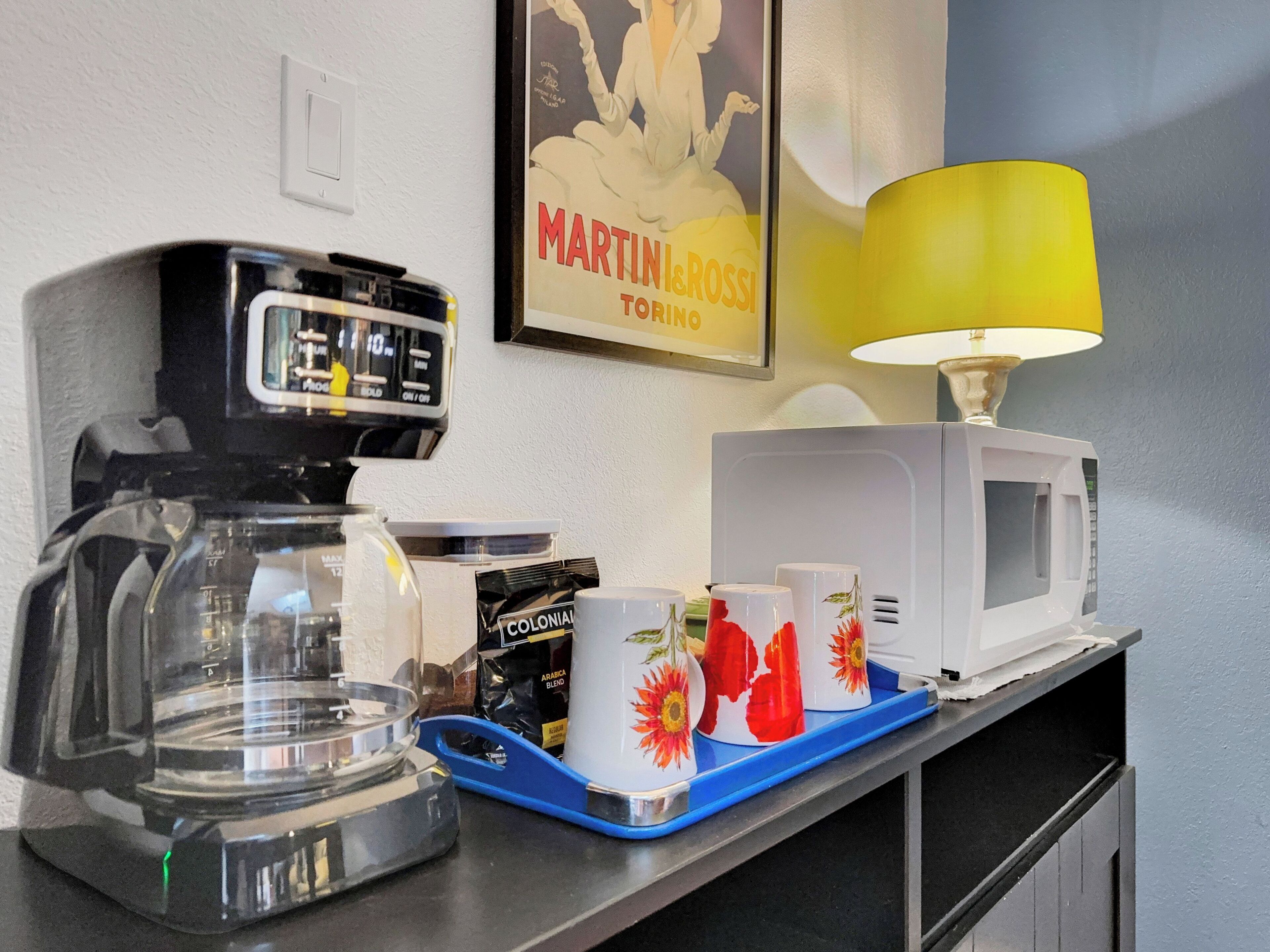A kitchenette with a coffee maker, a microwave, and a tray with cups.