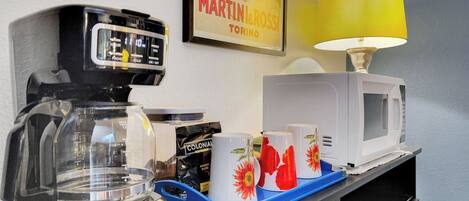A kitchenette with a coffee maker, a microwave, and a tray with cups.