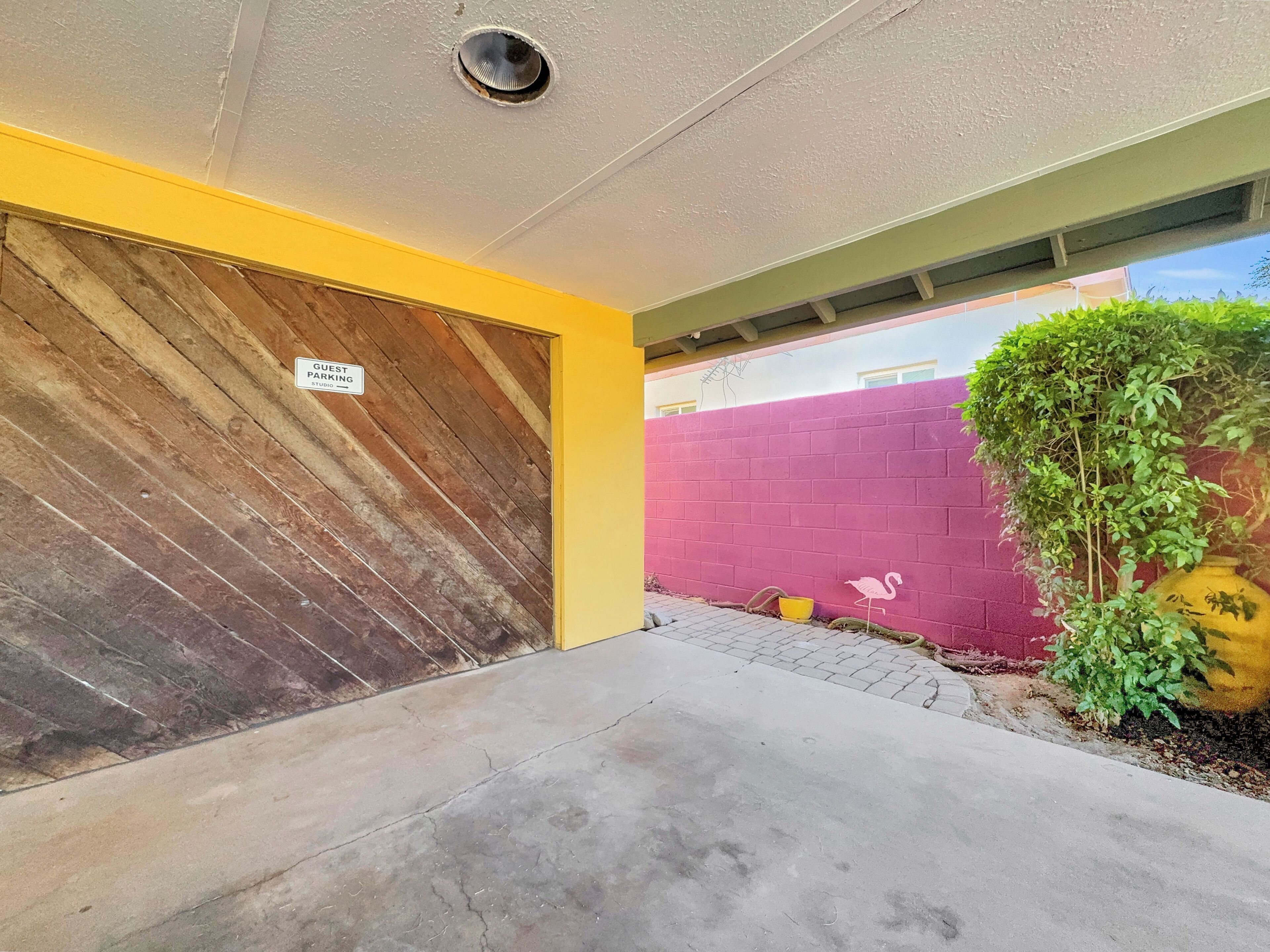 A building entrance with a wooden door, a 'Guest Parking' sign, a red wall, and a small plant.