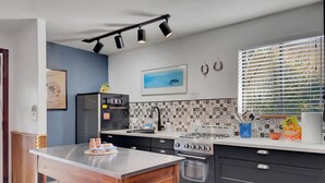 Une cuisine moderne dotée d’un îlot central, de meubles de couleur noire et d’un dosseret carrelé.