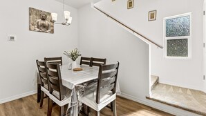 Comedor con mesa preparada para cuatro personas, sillas de madera, una araña y un cuadro de Buda en la pared.