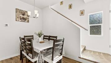 Un coin repas avec une table dressée pour quatre personnes, des chaises en bois, un lustre et un tableau représentant un Bouddha accroché au mur.