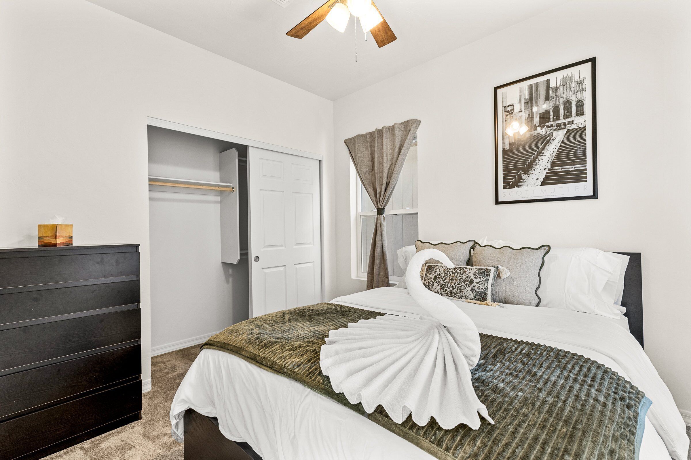 A hotel room with a bed, a dark wooden dresser, a white door, and a framed picture on the wall.