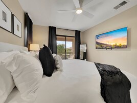 Quarto de hotel com uma cama grande, um ventilador de teto, uma TV na parede e vista para o exterior pela janela.