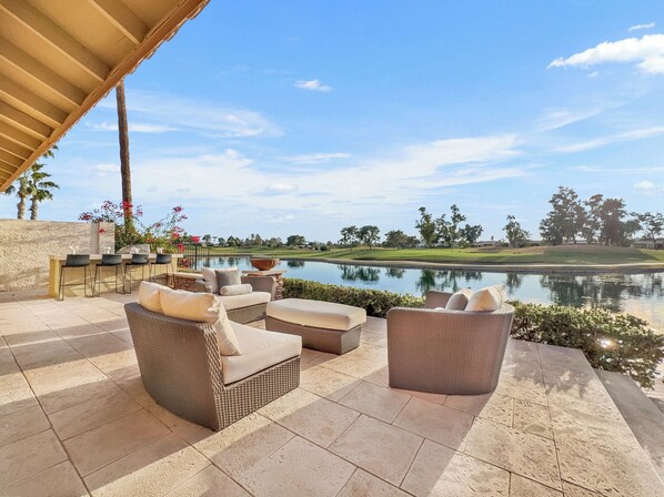 An outdoor patio with wicker furniture, a stone-tiled floor, and a view of a golf course and lake. - Oleander Chandler/ocotillo (Chandler)