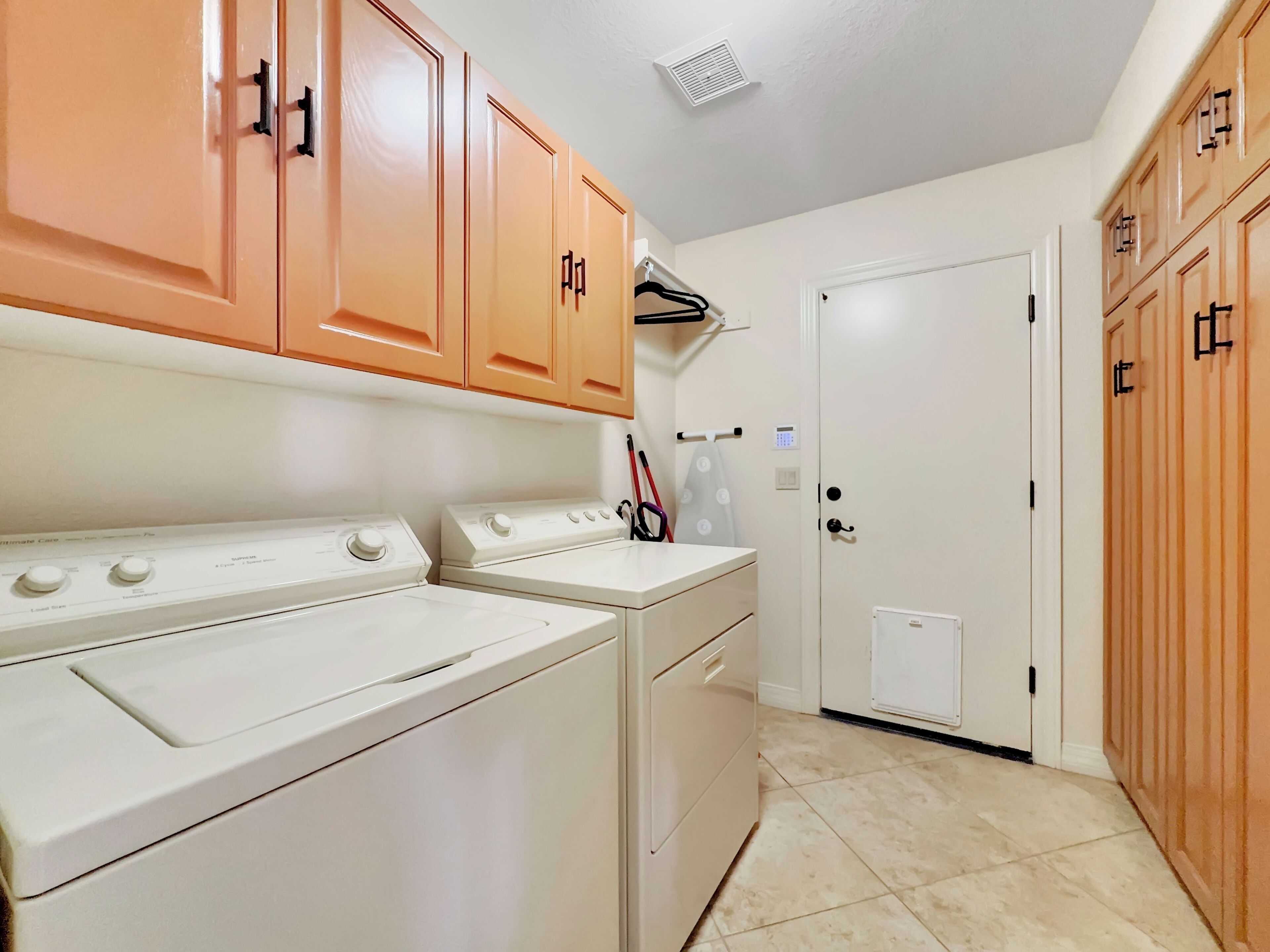 A laundry room with two white washing machines, a dryer, and wooden cabinets with black handles.