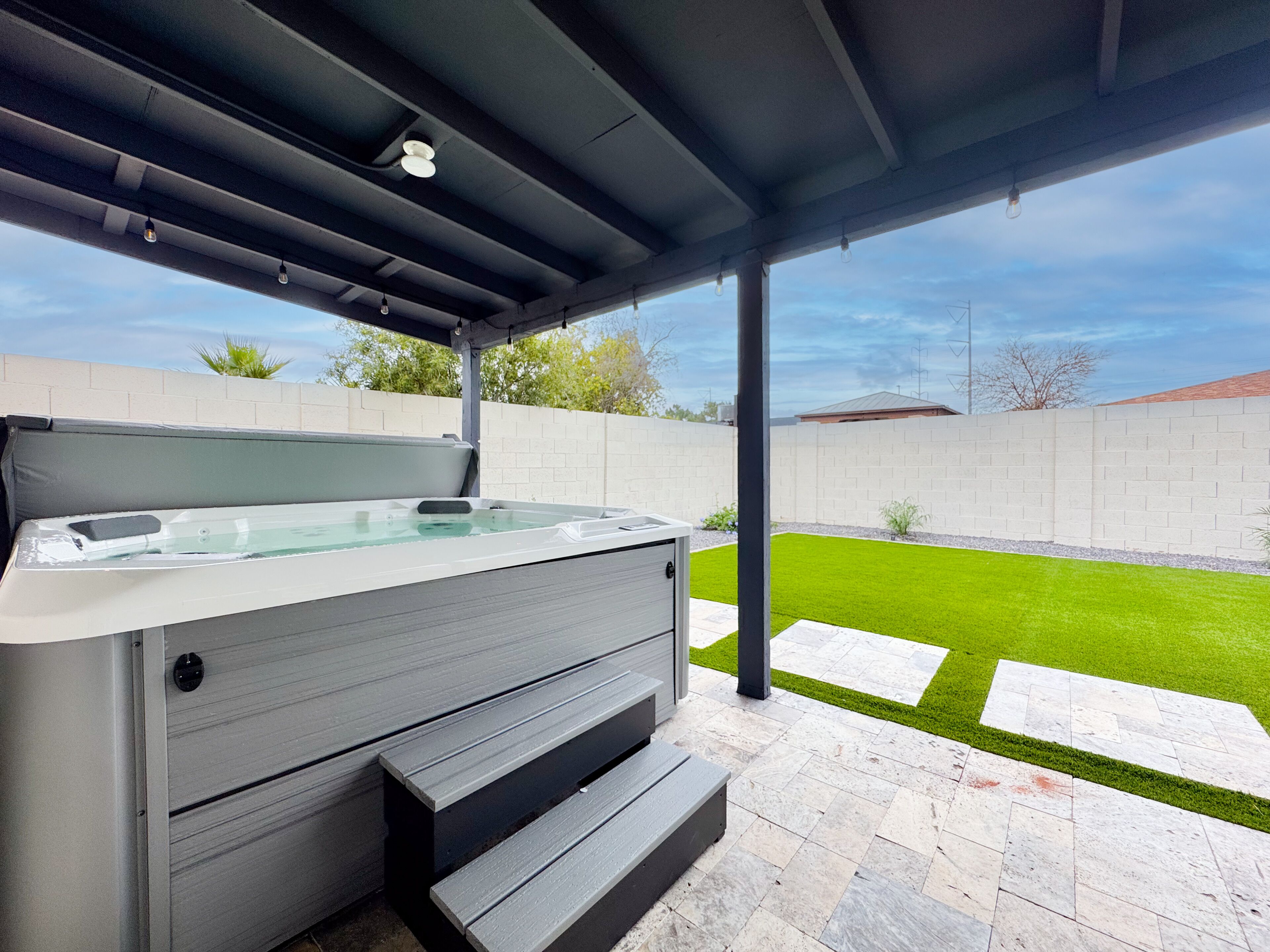 Een hottub onder een overdekt terras met een stenen vloer en een gazon.
